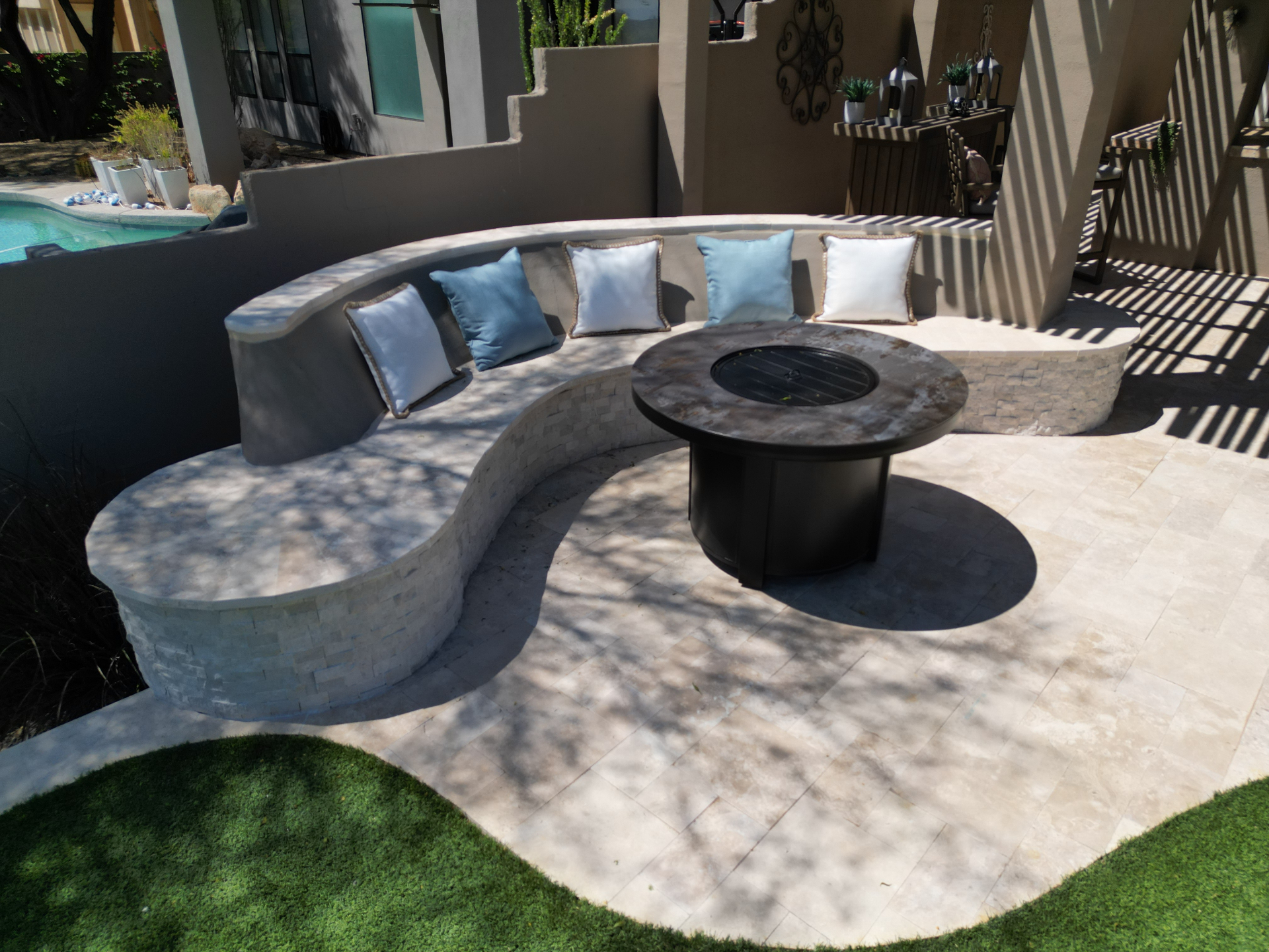 Curved stacked-stone bench and fire table on a travertine patio